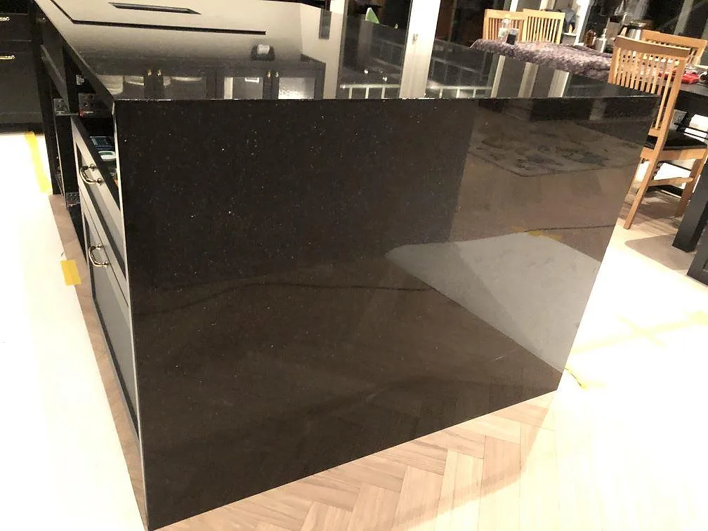 Nedvikt sidopanel på en köksö i polerad svart Star Galaxy granit som speglar rummet, i ett kök i Alingsås.