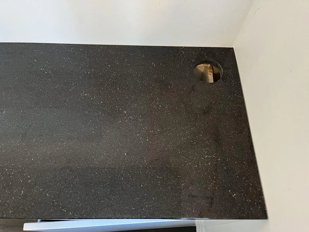 Närbild på polerad Star Galaxy granitbänkskiva med urtag för köksblandare, där de silvriga och bronsfärgade kristallerna syns tydligt, i ett kök i Göteborg.