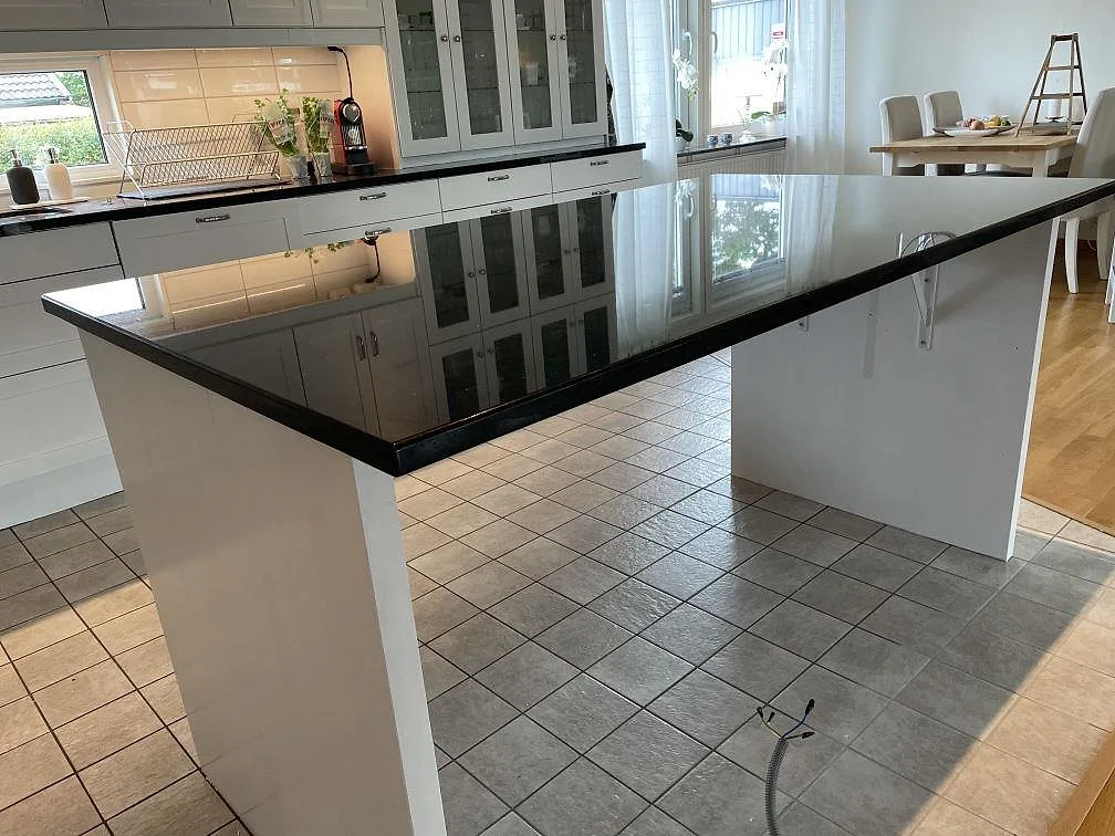 Stor köksö i polerad Star Galaxy granit på vit bas framför vita köksskåp och klinkergolv i Jonstorp.