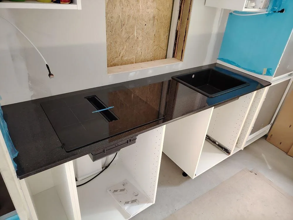 Köksbänkskiva i svart Star Galaxy granit, polerad, med hälluttag och diskho på vita köksstommar under montering i Kungsör.