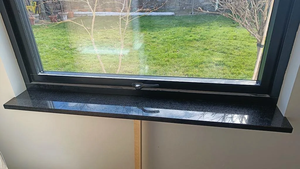 Fönsterbänk i polerad Star Galaxy granit monterad under svart fönsterkarm i Löddeköpinge.