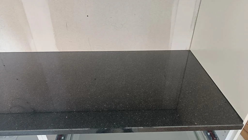 Köksbänkskiva i svart Star Galaxy granit, polerad, monterad i vinkel längs väggen i ett kök under installation i Trelleborg.