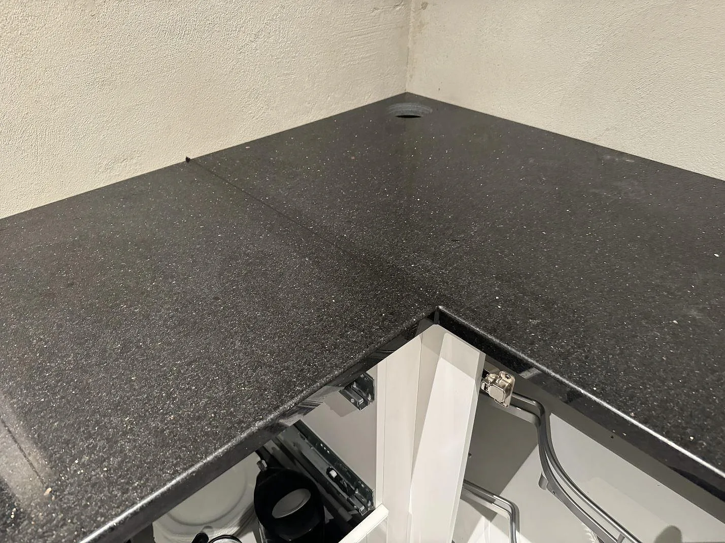 Hörn av L-formad köksbänkskiva i polerad Star Galaxy granit med rund kranöppning och vita stommar i Trelleborg.