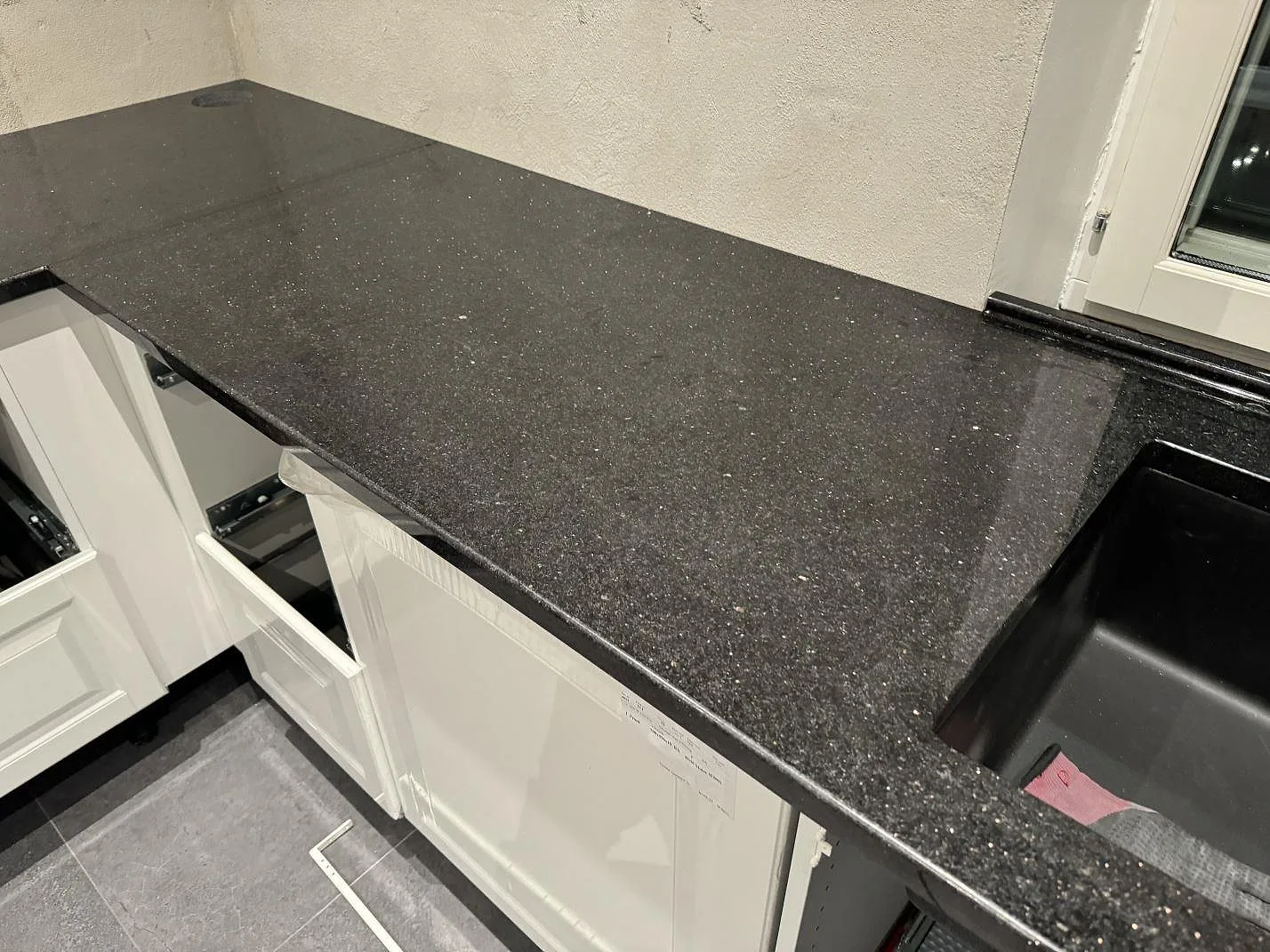 L-formad köksbänkskiva i polerad Star Galaxy granit med diskho, öppen vit stomme och monteringsdetaljer i Trelleborg.