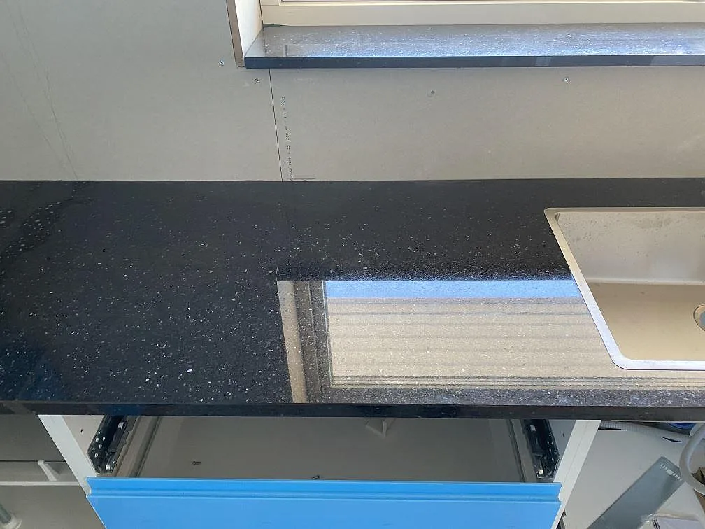 Köksbänkskiva i mörk granit Star Gate, polerad, med köksö och underlimmad diskho i ett U-format kök under montering i Älvängen.