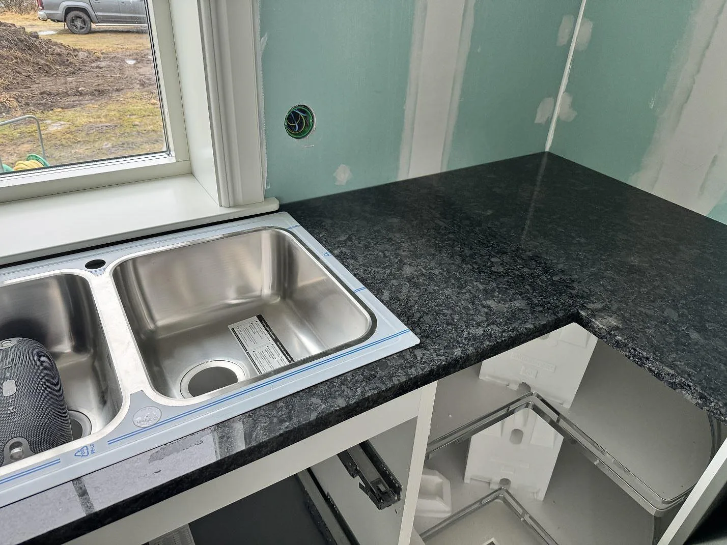 L-formad köksbänkskiva i polerad Steel Grey granit med rostfri dubbelho och mintgröna väggar i Älmestad.