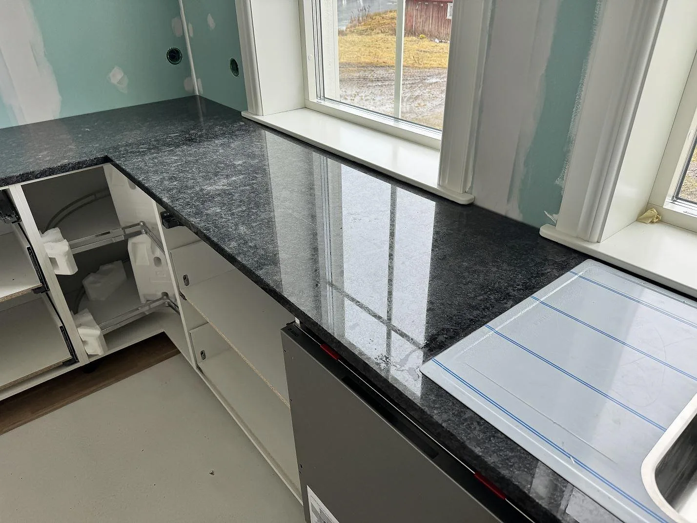 Köksbänkskiva i polerad Steel Grey granit vid stora fönster i ett kök under montering i Älmestad.