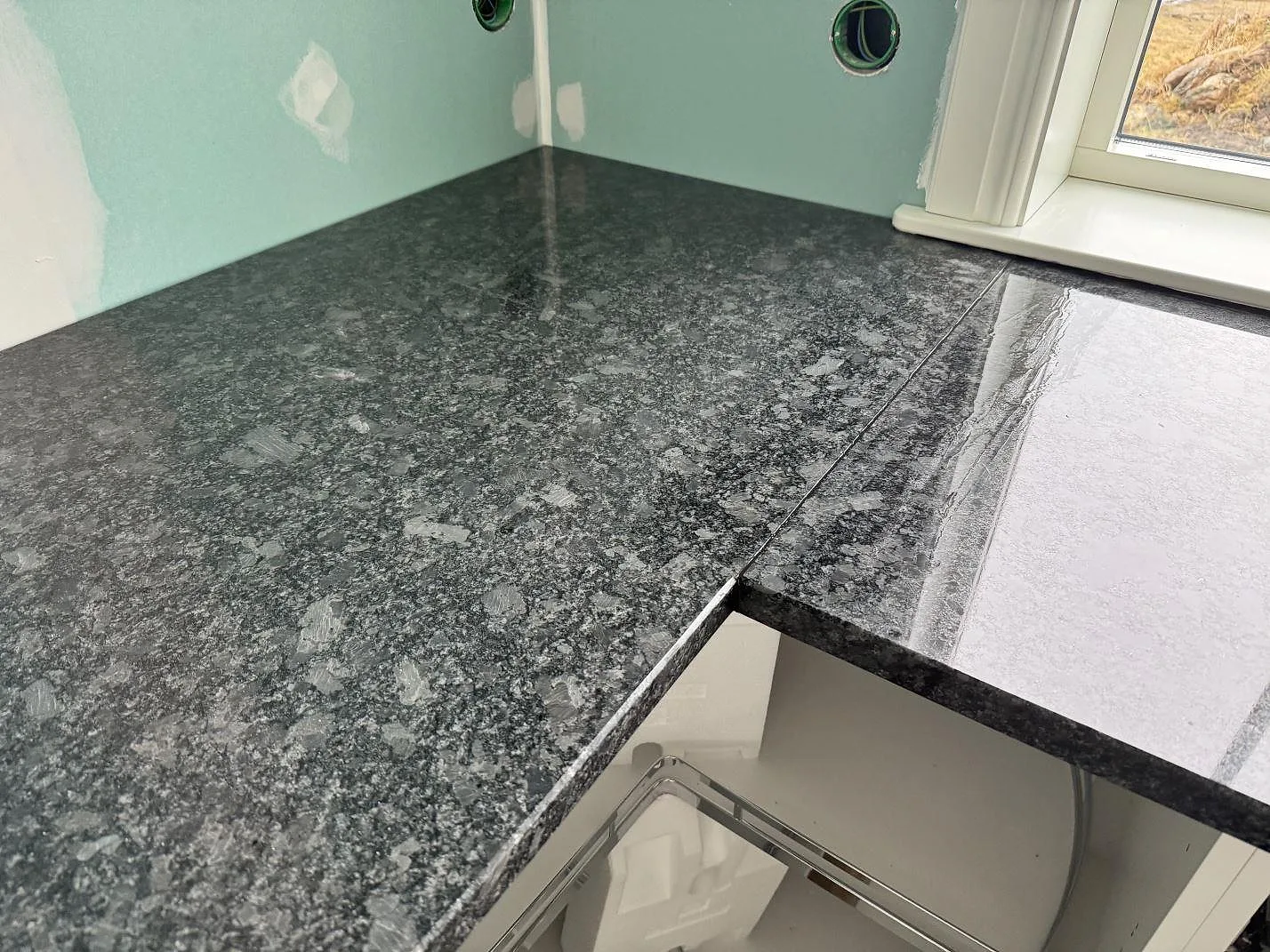 Detalj av den polerade Steel Grey granitens mörkgrå kristallmönster vid köksfönster i Älmestad.
