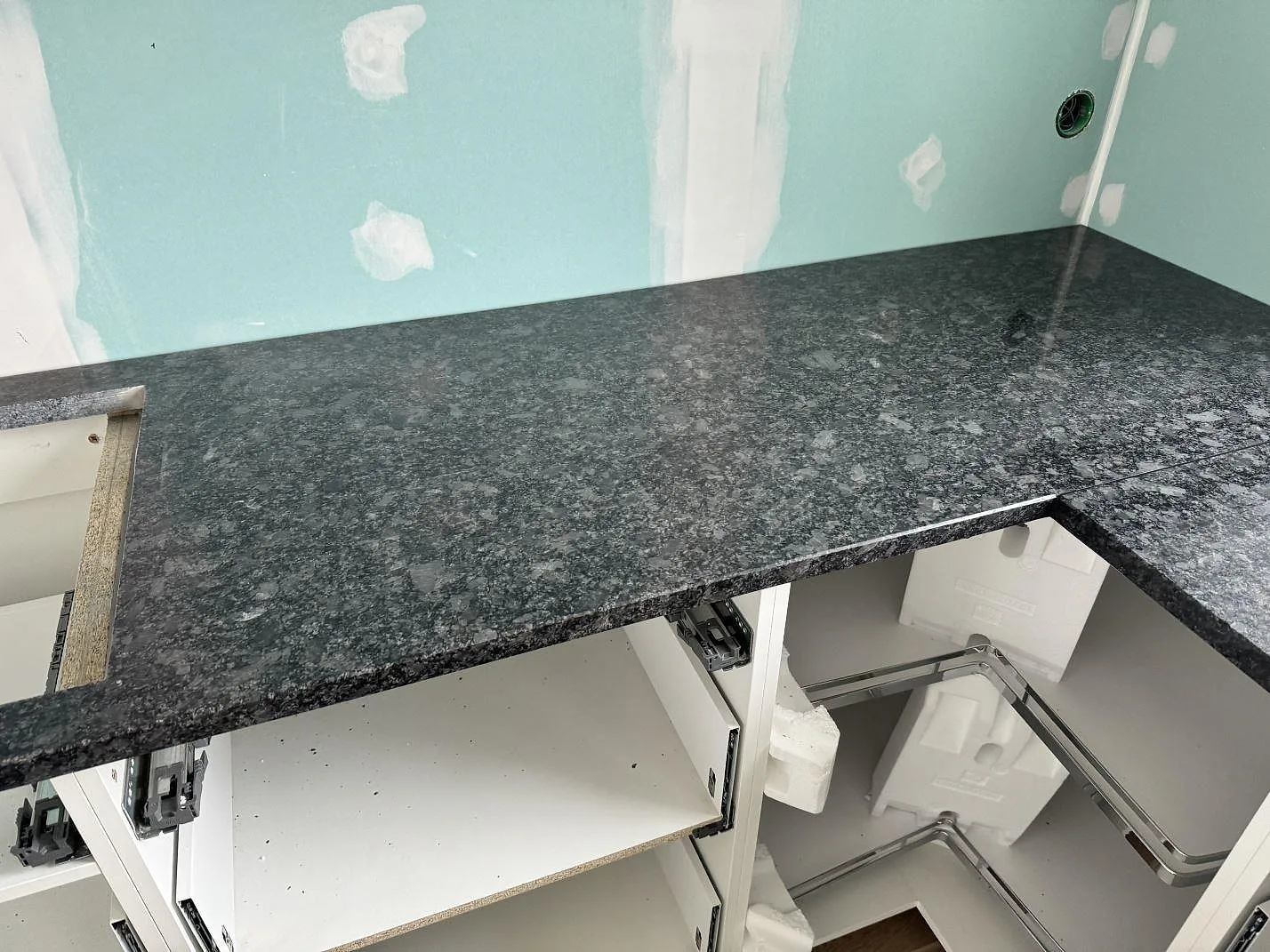 Lång köksbänk i polerad Steel Grey granit över öppna vita stommar under montering i Älmestad.
