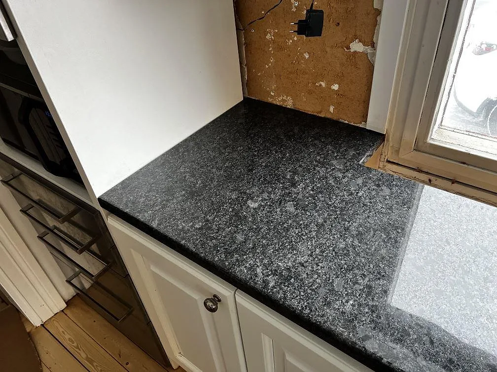 Närbild på polerad Steel Grey granit vid fönstret i ett kök i Borås, med tydlig mörk och ljus naturlig struktur.