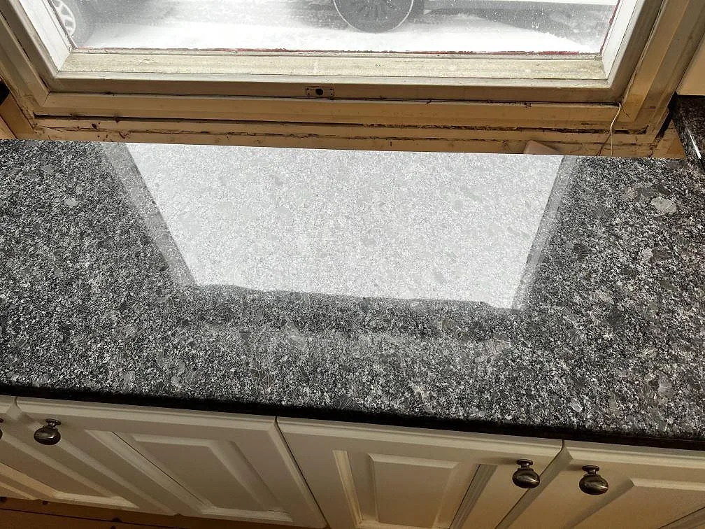 Fönstersträckning i polerad Steel Grey granit i Borås, fotograferad ovanifrån med spegling från fönstret i stenytan.