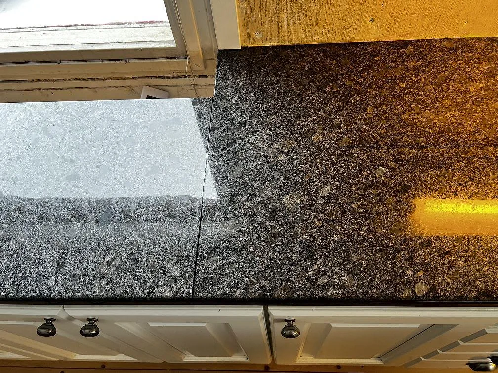 Skarv och yta i polerad Steel Grey granit på köksbänkskiva i Borås, med varm arbetsbelysning över stenen.