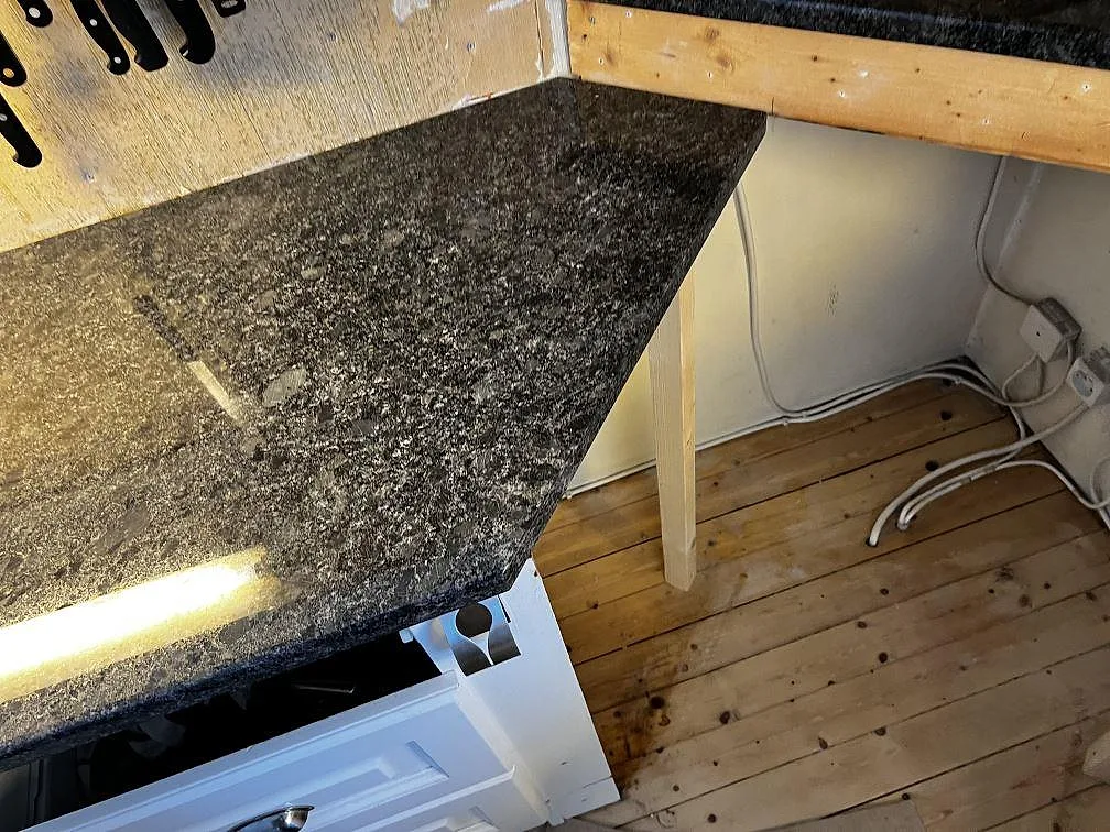 Vinklad del av köksbänkskiva i polerad Steel Grey granit intill fristående spis och trägolv i Borås.