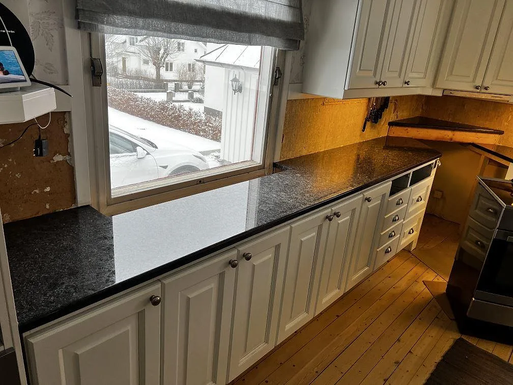 Polerad Steel Grey granit som köksbänkskiva längs fönstret, med mörk spegling i stenen och vita köksluckor i Borås.