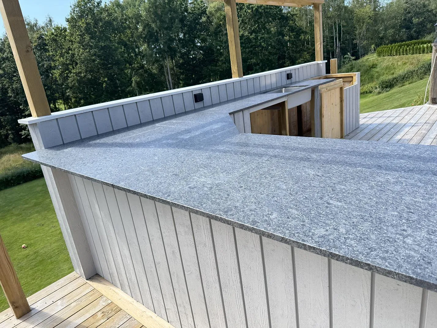 Närbild av matt Steel Grey granit som köksbänkskiva i ett utekök i Fjärås, med diskhozon längre bort.