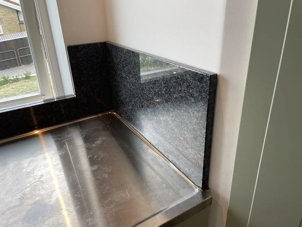 Detalj av Steel Grey granit som stänkskydd vid diskbänken och fönstret i ett kök i Flyinge.