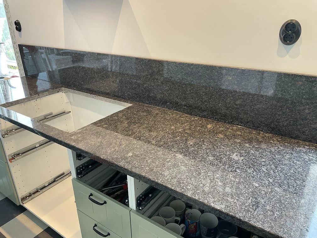 Steel Grey granit som köksbänkskiva med stänkskydd och öppna skåpstommar under montering i Flyinge.