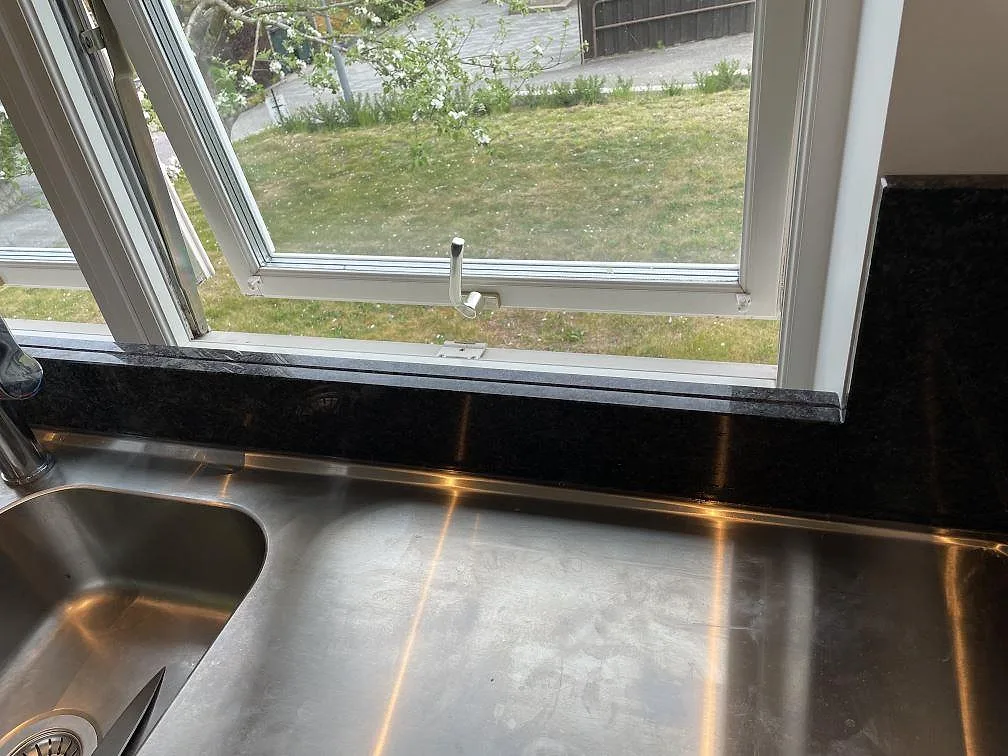 Fönsterdetalj med Steel Grey granit som stänkskydd och smal bänkkant vid diskbänken i Flyinge.