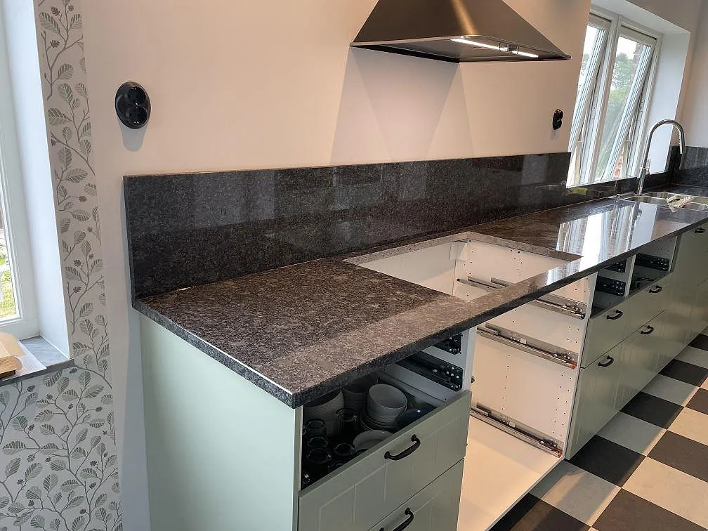 Köksbänkskiva i Steel Grey granit med polerad yta, stänkskydd och hälluttag i ett kök i Flyinge.