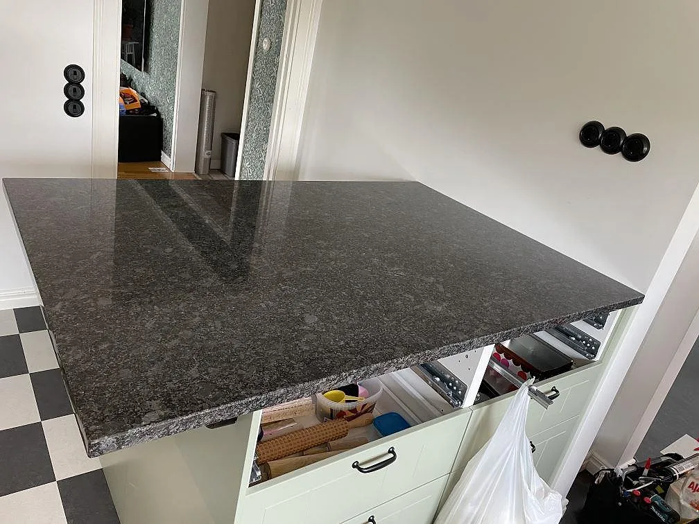 Köksö eller större bänkyta i Steel Grey granit med polerad yta på ljusgröna skåp i Flyinge.