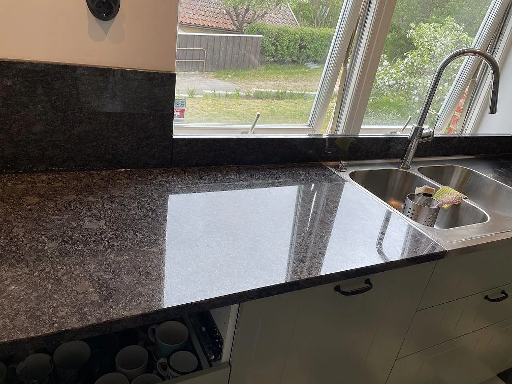 Köksbänkskiva i Steel Grey granit med blank yta vid diskbänkszonen och fönstret i Flyinge.