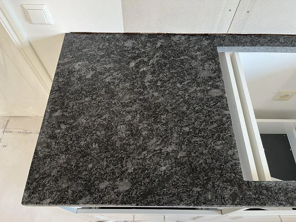 Hörn av Steel Grey granitbänkskiva i matt yta mot vit köksstomme i ett kök i Frillesås.
