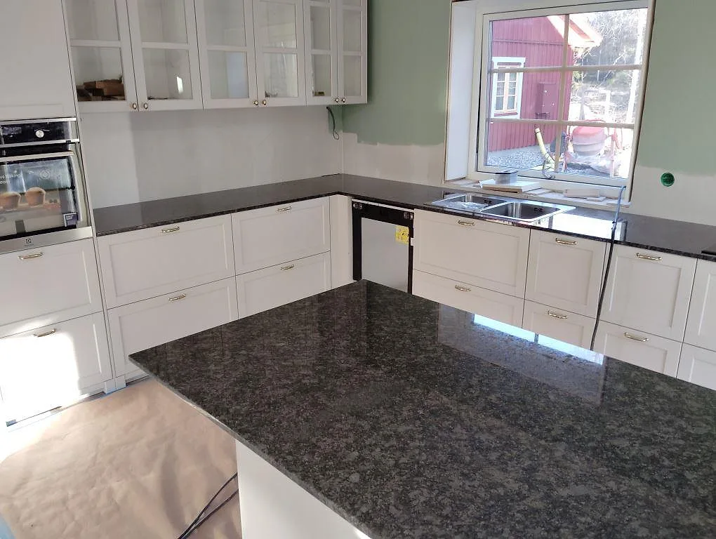 Köksbänkskiva i polerad Steel Grey granit med köksö och synlig diskho i ett kök i Glanshammar.