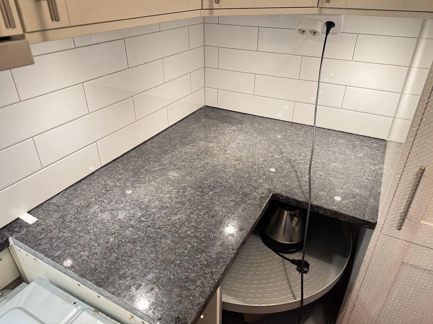 Polerad köksbänkskiva i Steel Grey granit runt ett hörn med vitt kakel och öppen stomme i Glommen.