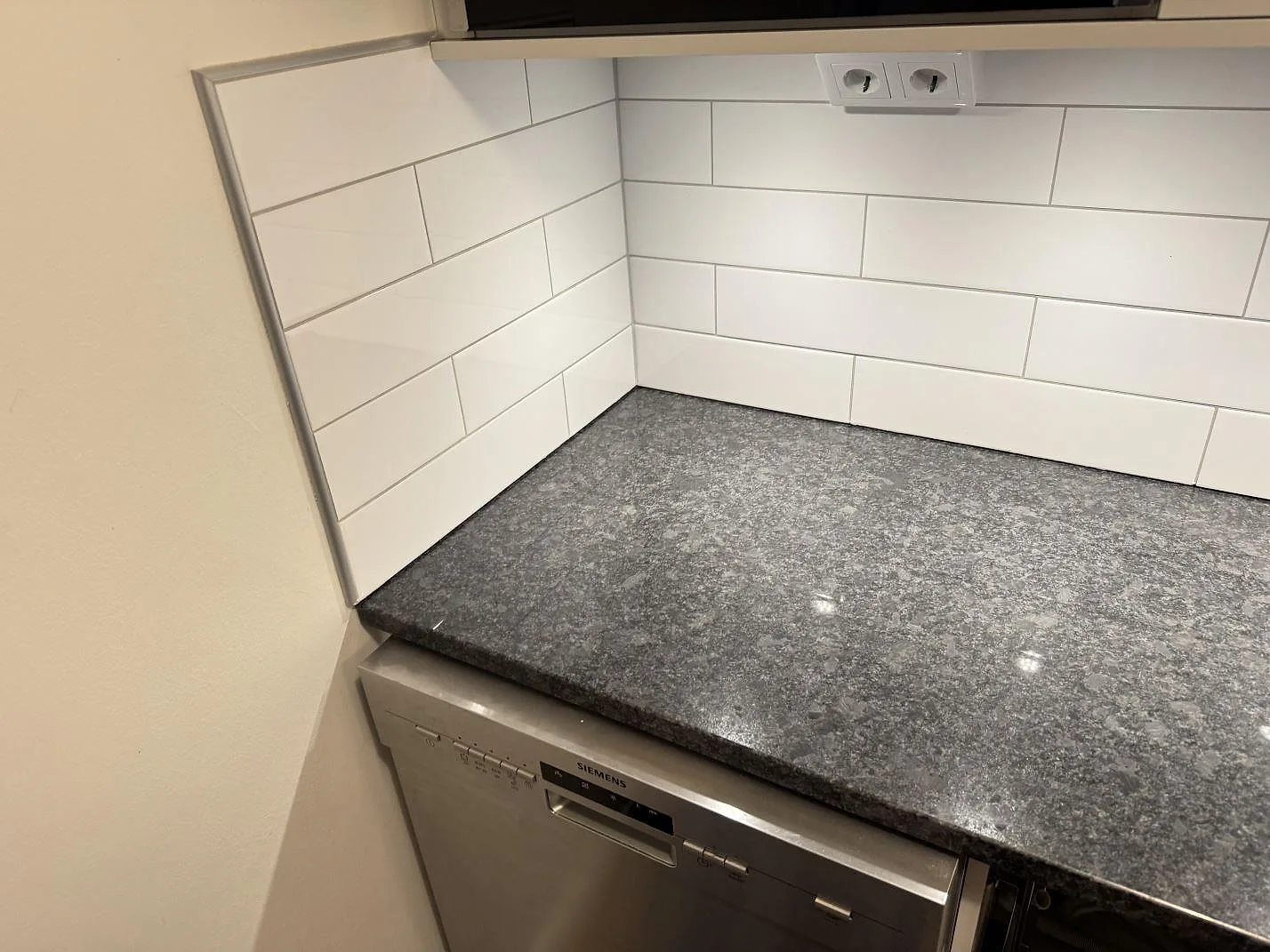 Hörnsektion av köksbänkskiva i polerad Steel Grey granit ovanför diskmaskin i Glommen.