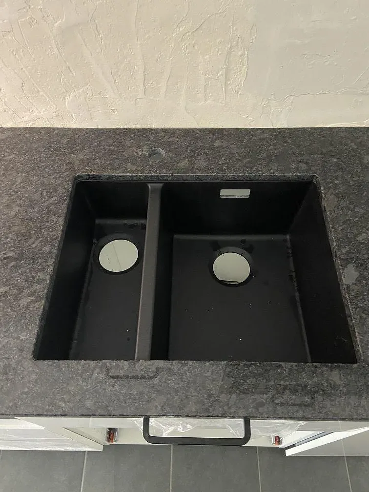 Närbild på underlimmad svart kompositdiskho med dubbla hoar under en Steel Grey-granitskiva i ett kök i Göteborg.