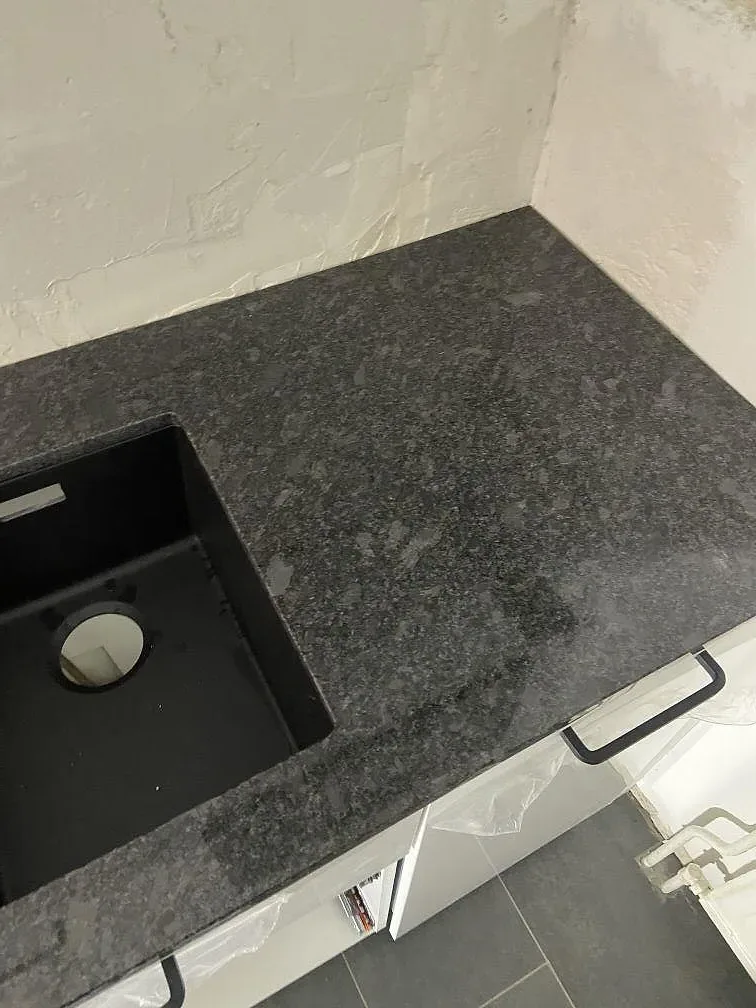 Bänkskiva i Steel Grey-granit med underlimmad svart dubbelho i komposit och borrat hål för köksblandare i ett kök i Göteborg.