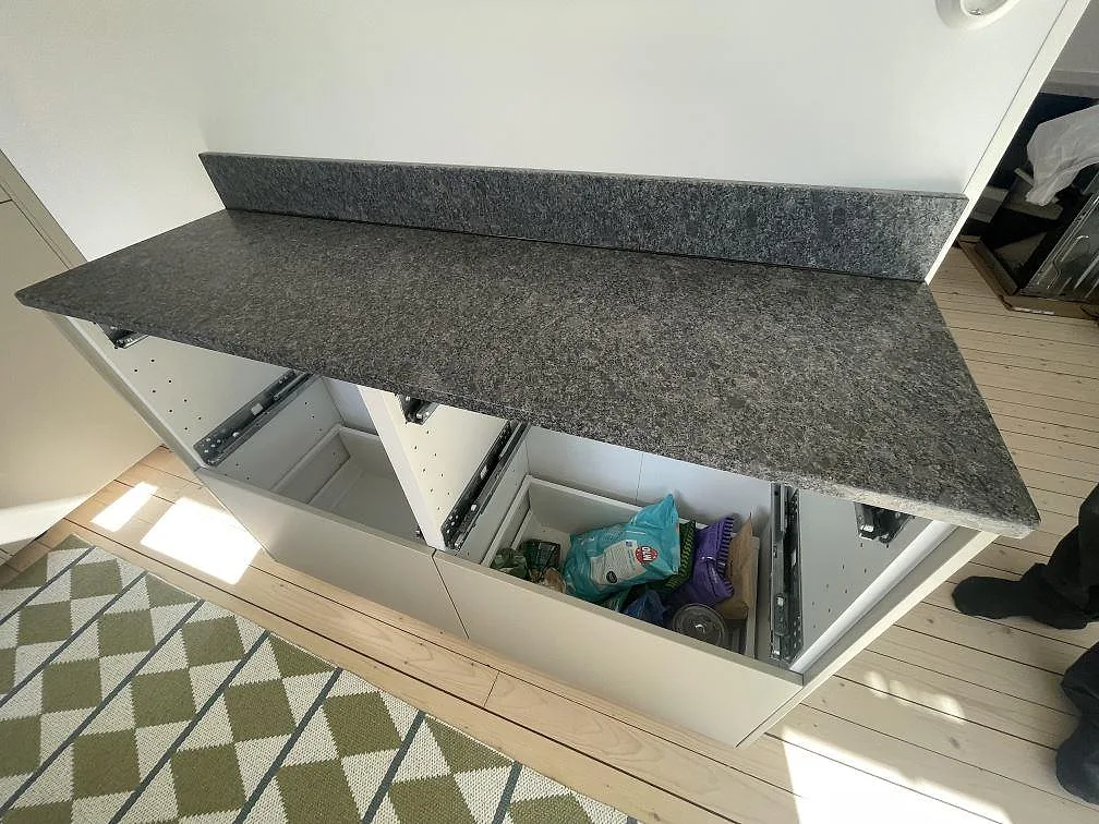 Sidobänk i matt Steel Grey granit med uppvikt stänkkant över vita köksstommar i Grisslehamn.