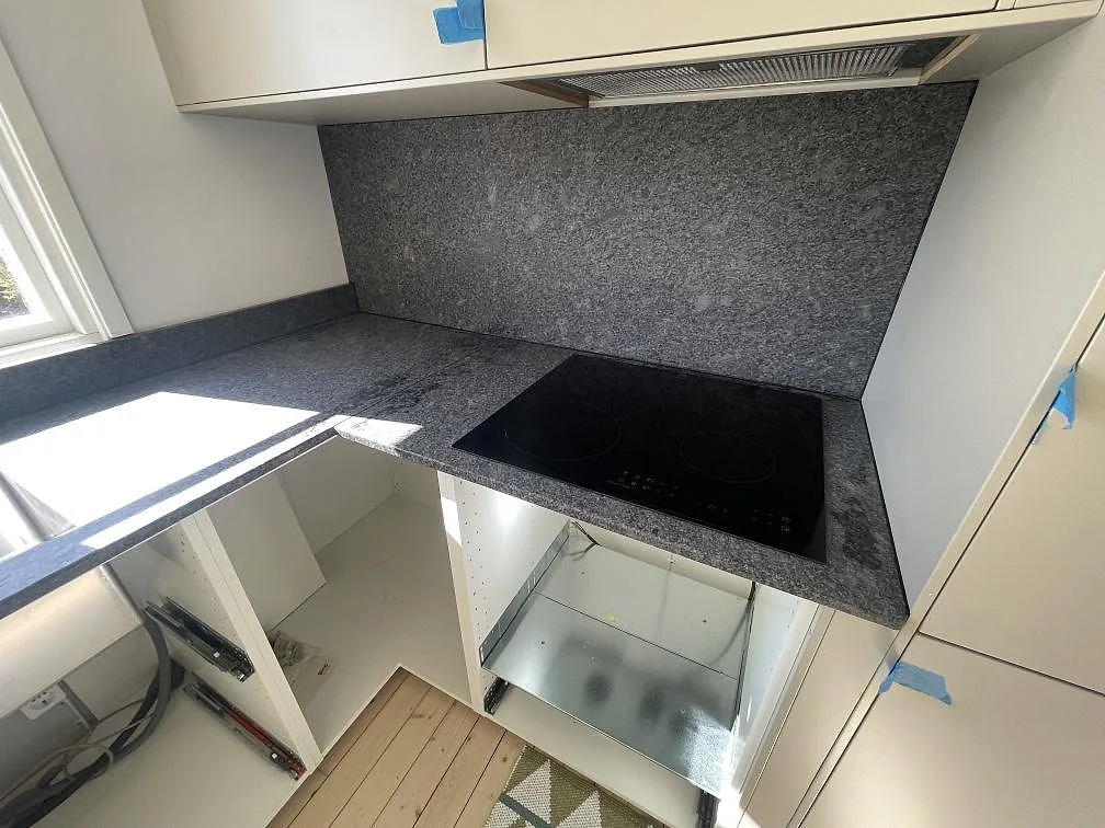 Hällzon i matt Steel Grey granit med stänkskydd bakom induktionshäll i ett kök i Grisslehamn.