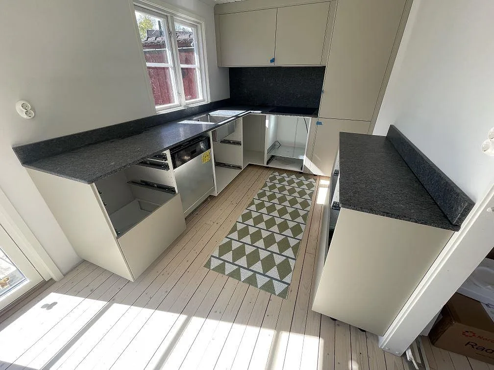 Köksbänkskivor i matt Steel Grey granit med uppvikt stänkkant, häll och synlig hoöppning i ett kök i Grisslehamn.