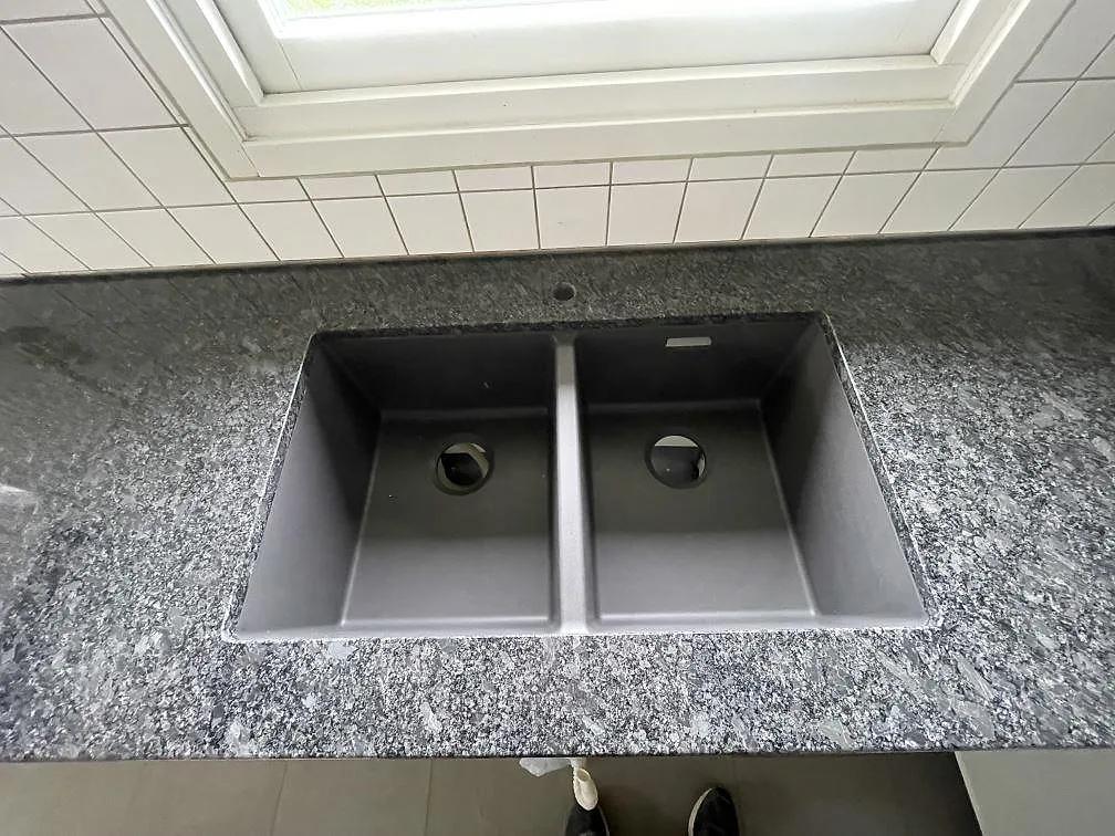 Dubbel underlimmad kompositdiskho i grått i en köksbänkskiva av Steel Grey granit under fönstret i ett kök i Halmstad.
