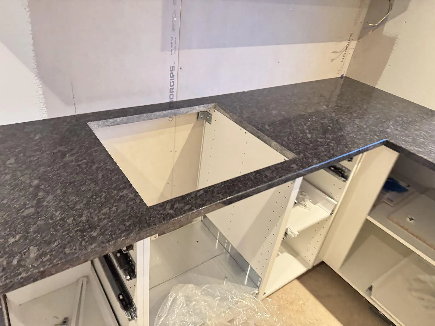 Vinklad bänkskiva i polerad Steel Grey-granit med hällurtag och mörk stenfront i ett kök i Haverdal.