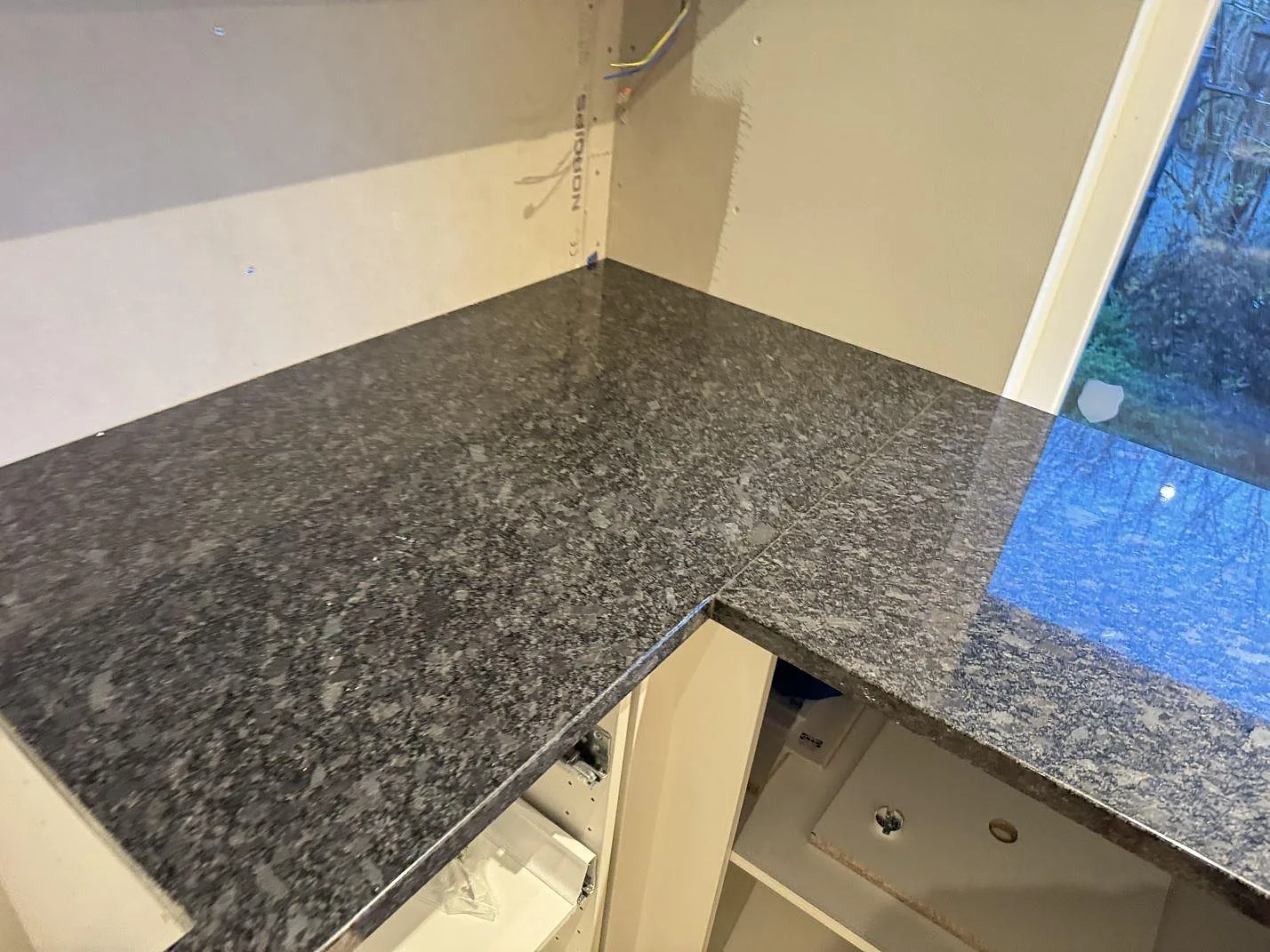 Hörndel i polerad Steel Grey-granit med blank yta och grå kristaller vid fönster i köket i Haverdal.