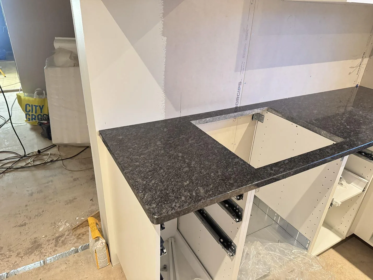 Polerad köksbänkskiva i Steel Grey-granit med rektangulärt hällurtag och öppna köksstommar under montering i Haverdal.
