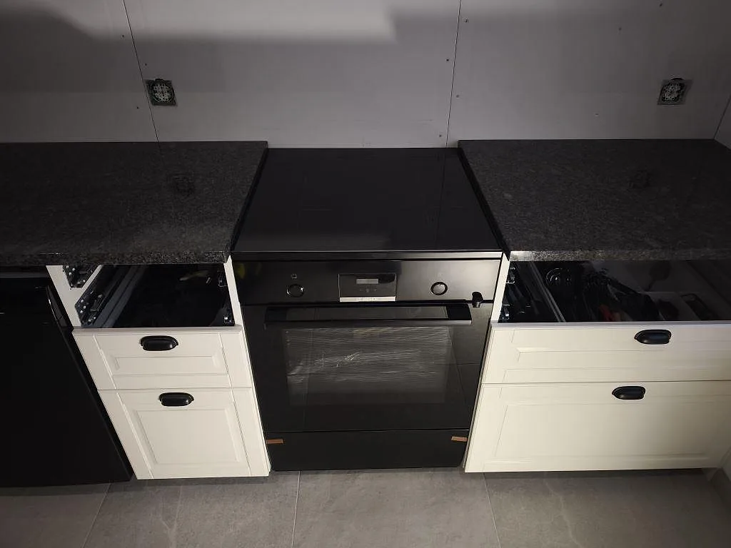 Köksbänkskivor i polerad Steel Grey granit runt svart spis och ugn i ett kök under montering i Helsingborg.