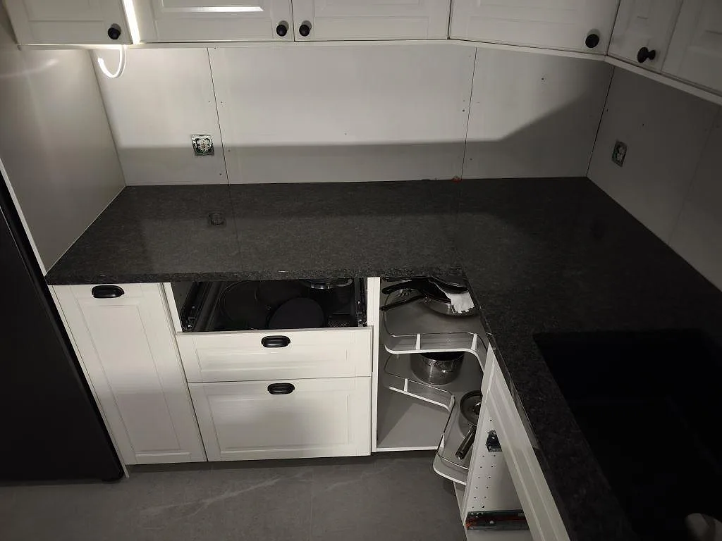 L-formad köksbänkskiva i polerad Steel Grey granit med mörk diskho och öppna stommar under montering i Helsingborg.