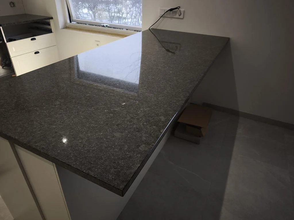 Polerad Steel Grey granit som köksbänkskiva med blank arbetsyta vid fönster i ett kök i Helsingborg.