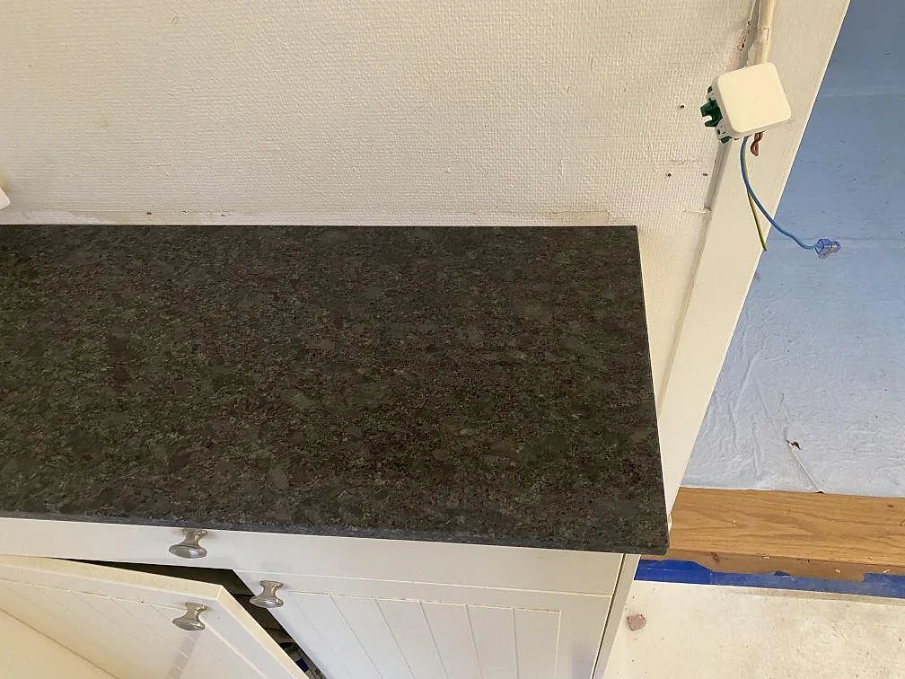 Installerad köksbänkskiva i Steel Grey granit längs köksvägg med tegelstänkskydd i Hindås.