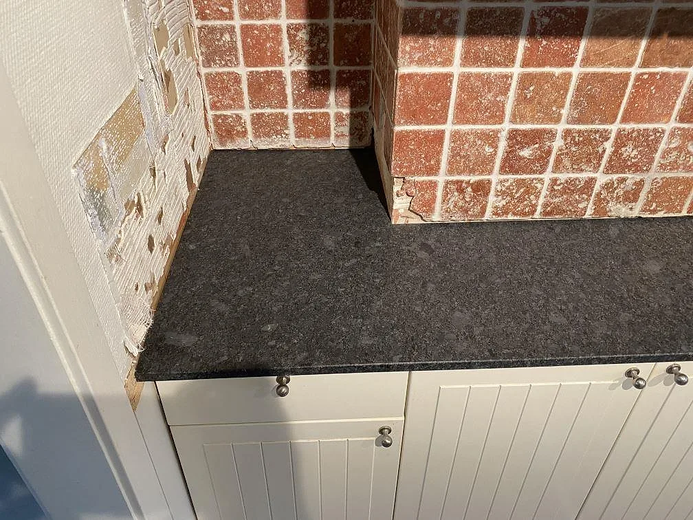 Mörkgrå Steel Grey granitbänkskiva mot tegelfärgat stänkskydd i ett kök i Hindås.