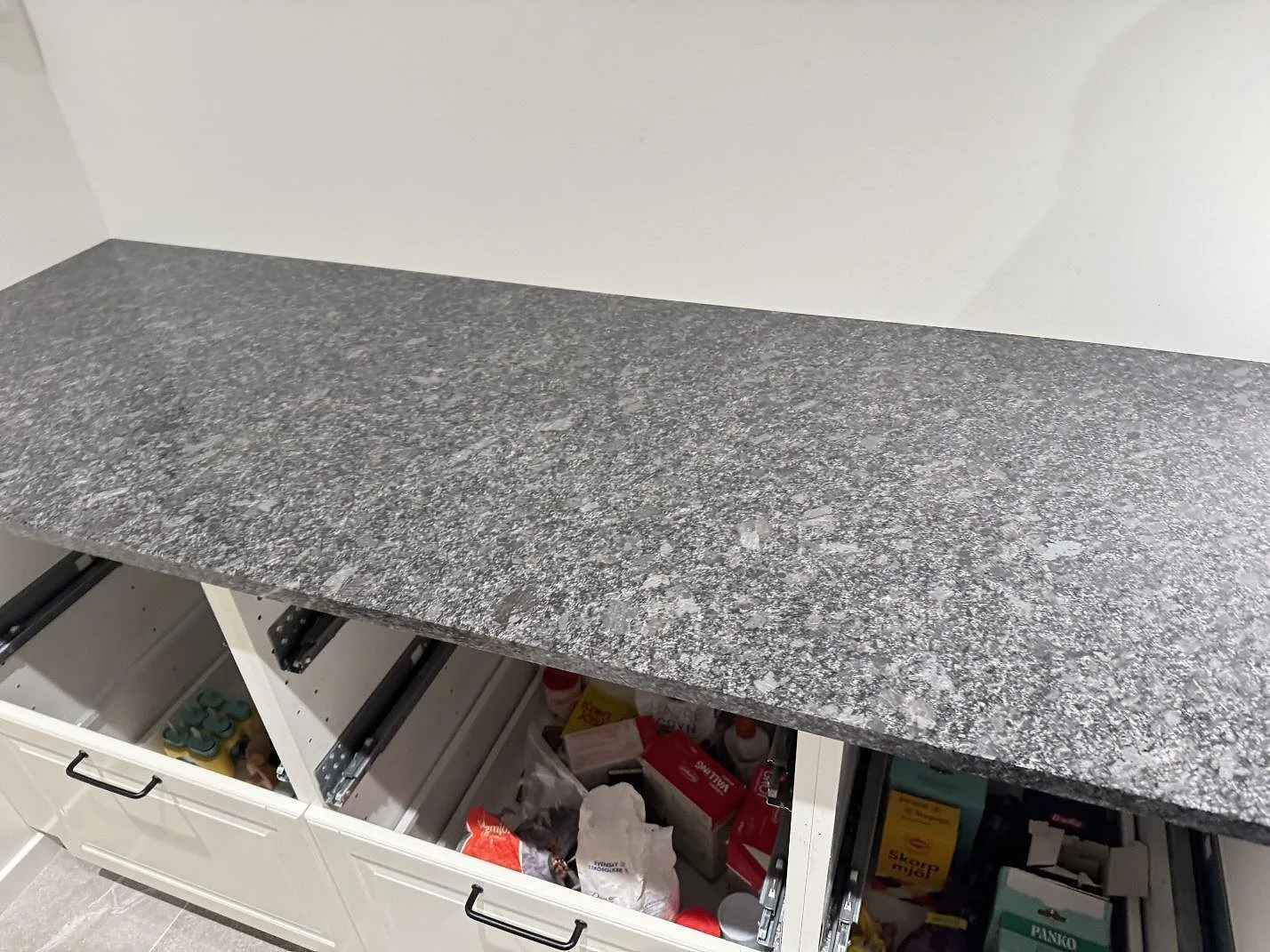 Närbild på den polerade ytan och den spräckliga grå ådringen i en Steel Grey-granitbänkskiva i ett kök i Kävlinge.