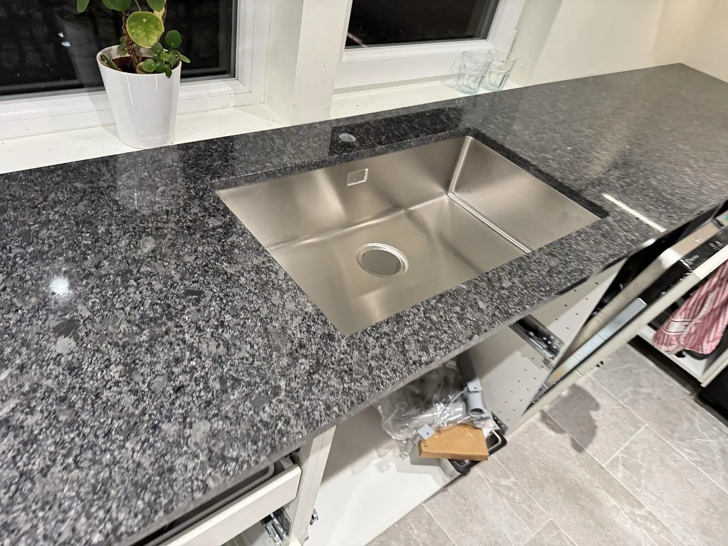 Stor underlimmad rostfri diskho i en polerad köksbänkskiva i Steel Grey-granit i ett kök i Kävlinge.