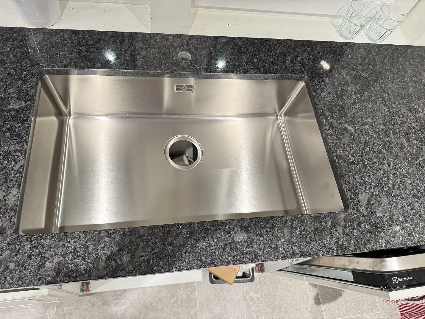 Underlimmad rostfri diskho sedd ovanifrån i en polerad Steel Grey-granitbänkskiva i ett kök i Kävlinge.