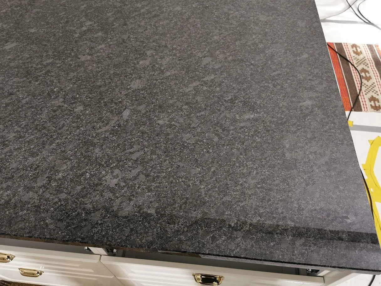 Köksbänkskiva i Steel Grey granit monterad på vita lådfronter, polerad mörkgrå yta i ett kök i Knisslinge.