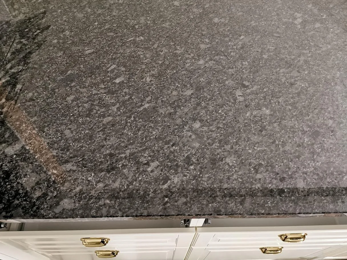 Närbild på den spräckliga ytan av en köksbänkskiva i polerad Steel Grey granit i ett kök i Knisslinge.