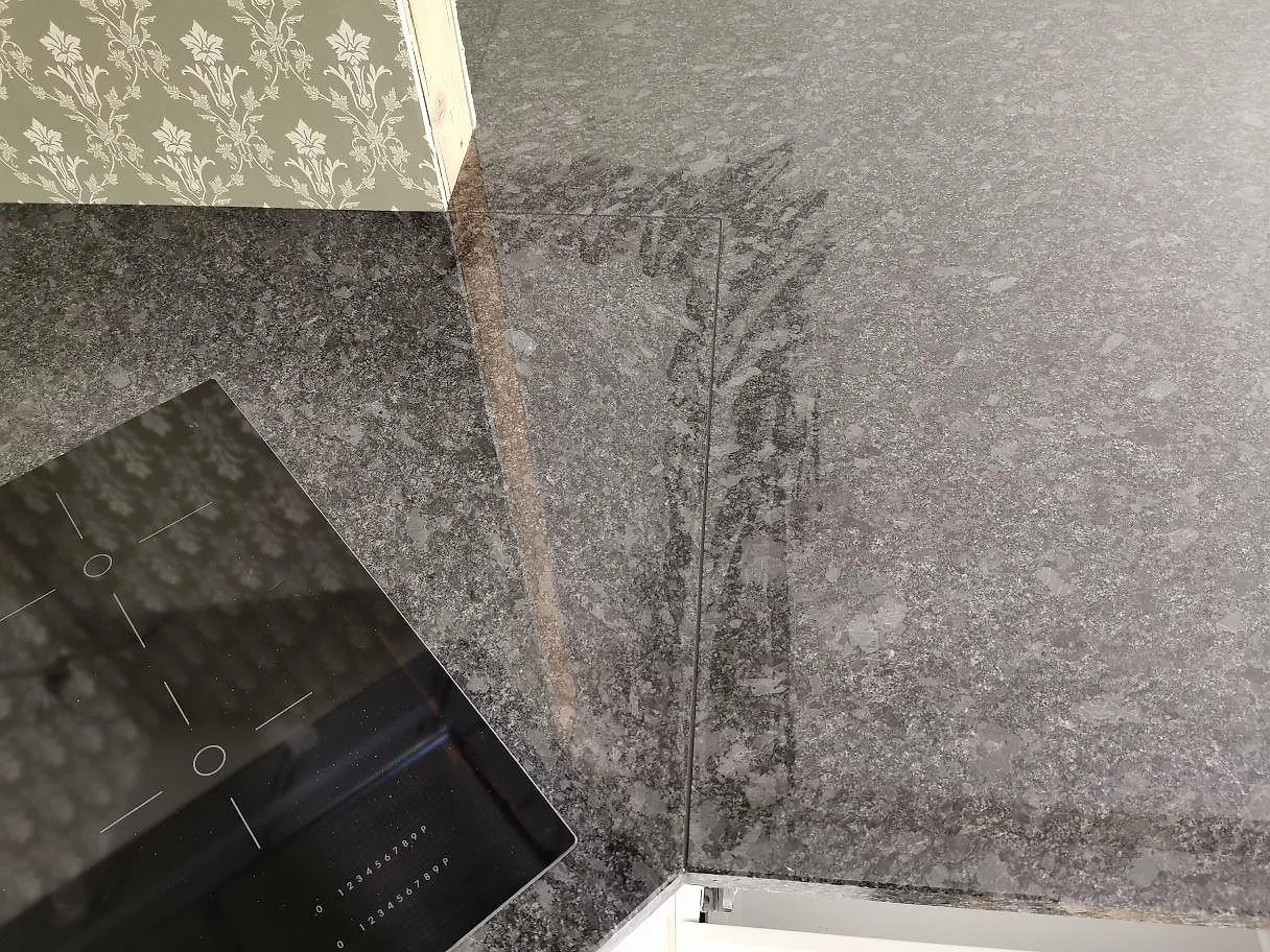 Köksbänkskiva i Steel Grey granit med plats för en övermonterad häll, polerad mörkgrå sten i ett kök i Knisslinge.