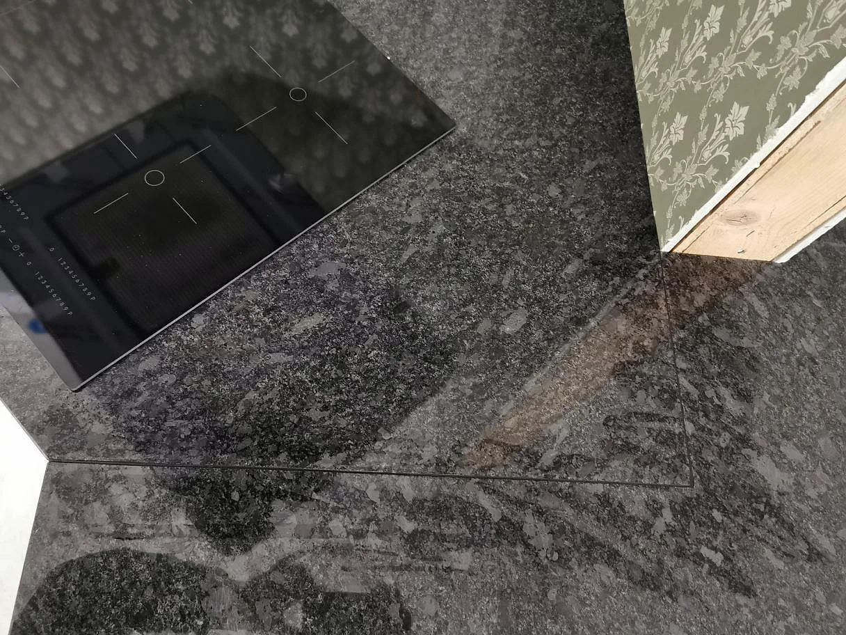 Köksbänkskiva i polerad Steel Grey granit med hällyta och spräcklig grå struktur i ett kök i Knisslinge.